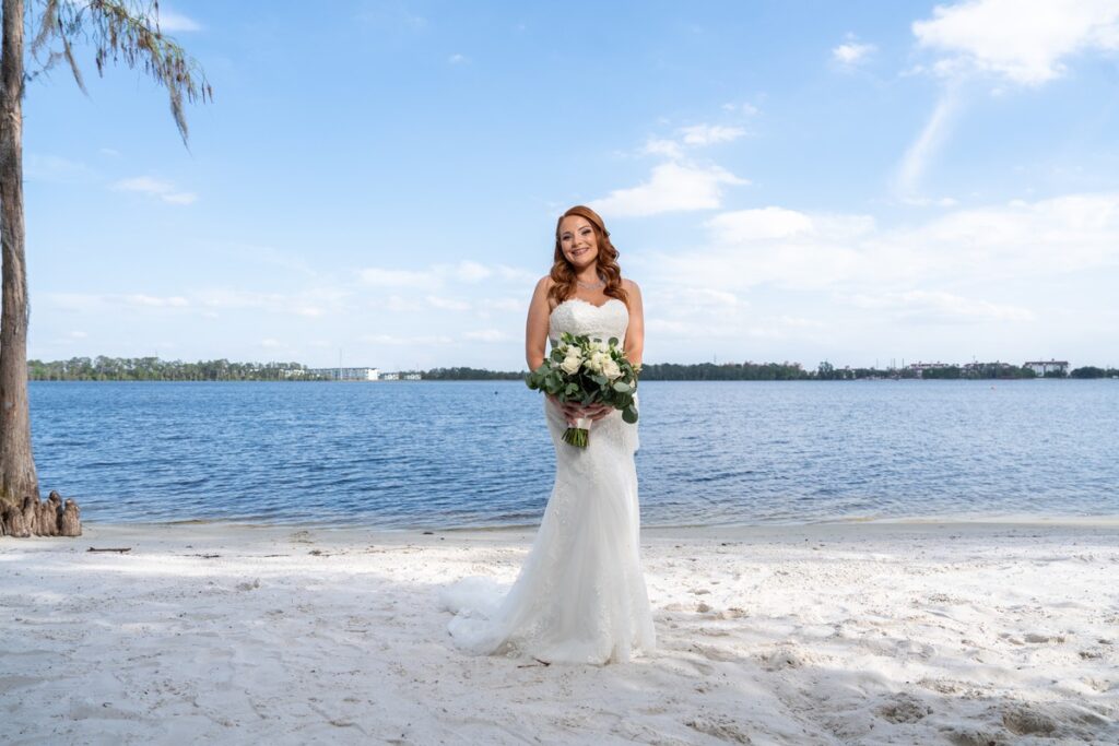 A bride holding a bouquet on a sandy beach beside a Central Florida lake