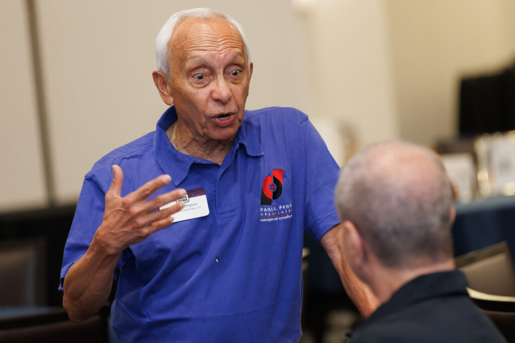 A guest in a blue polo shirt speaking with another attendee